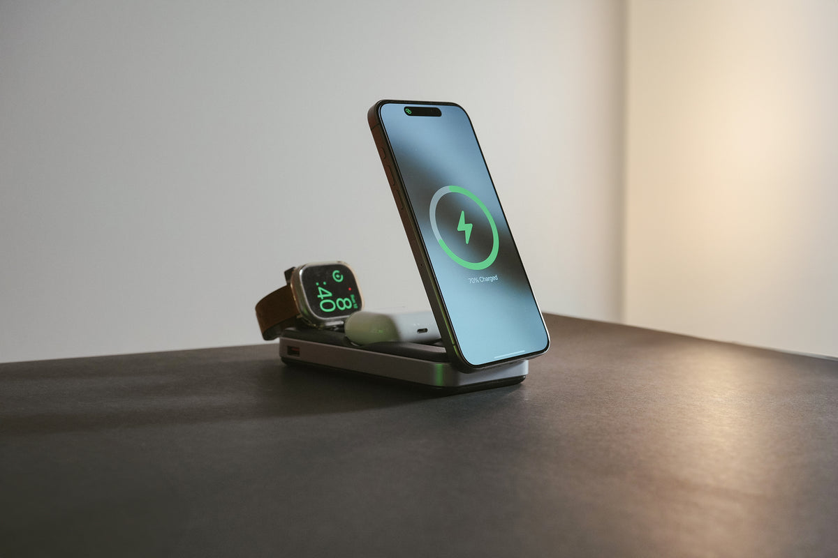A smartphone and a smartwatch are charging on a dual wireless charging stand. The phone screen displays a green charging icon.