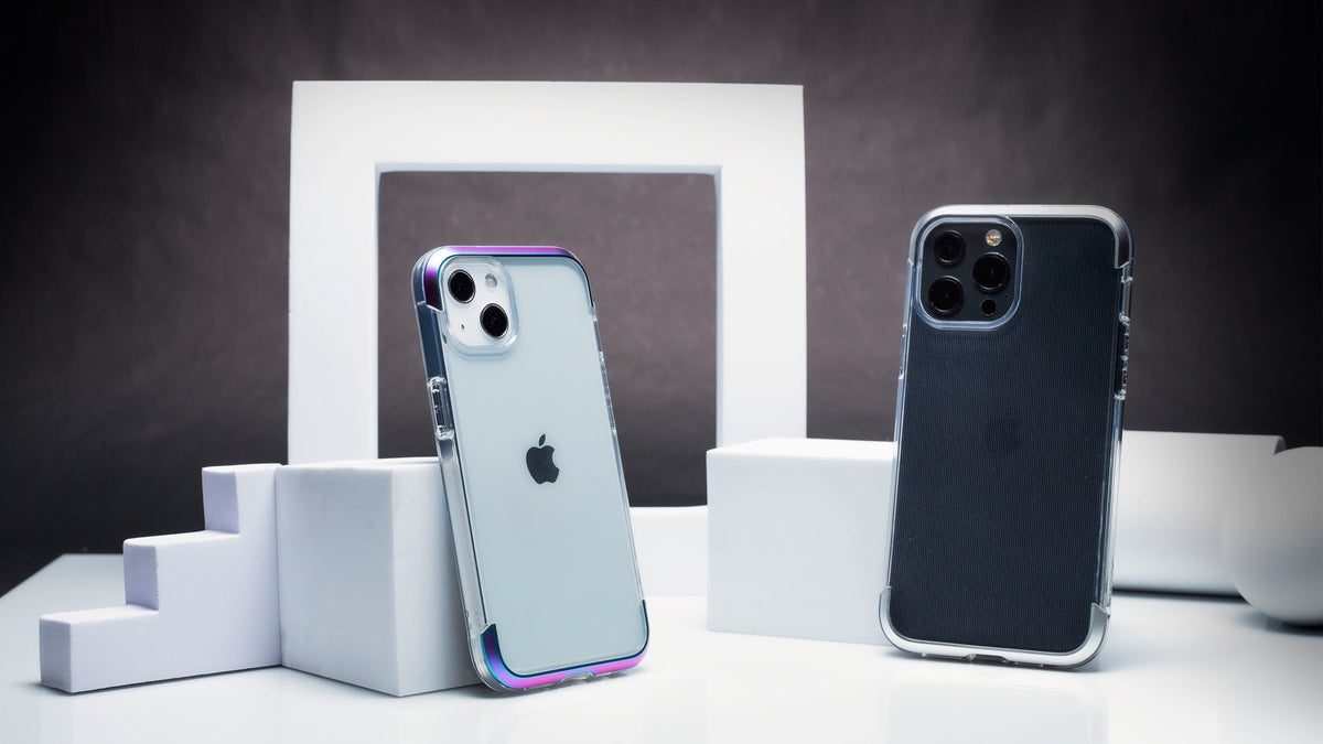 Two smartphones with cases propped against white geometric shapes on a table with a neutral background.