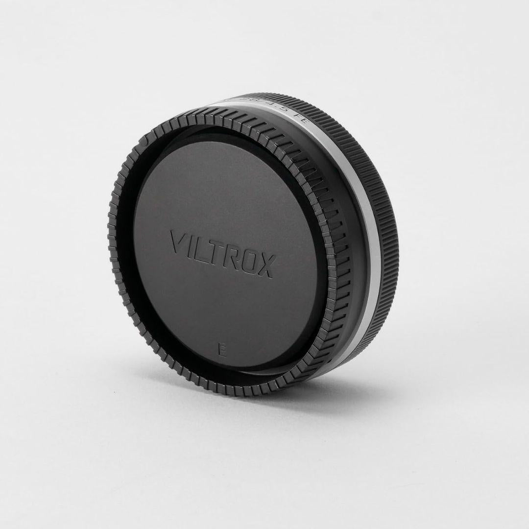A black Viltrox lens cap for the Viltrox 28mm f/4.5 FE (Sony Full Frame) stands upright on a white background. The cap features a ridged edge for grip and "VILTROX" embossed in the center, with even lighting and soft shadows below.