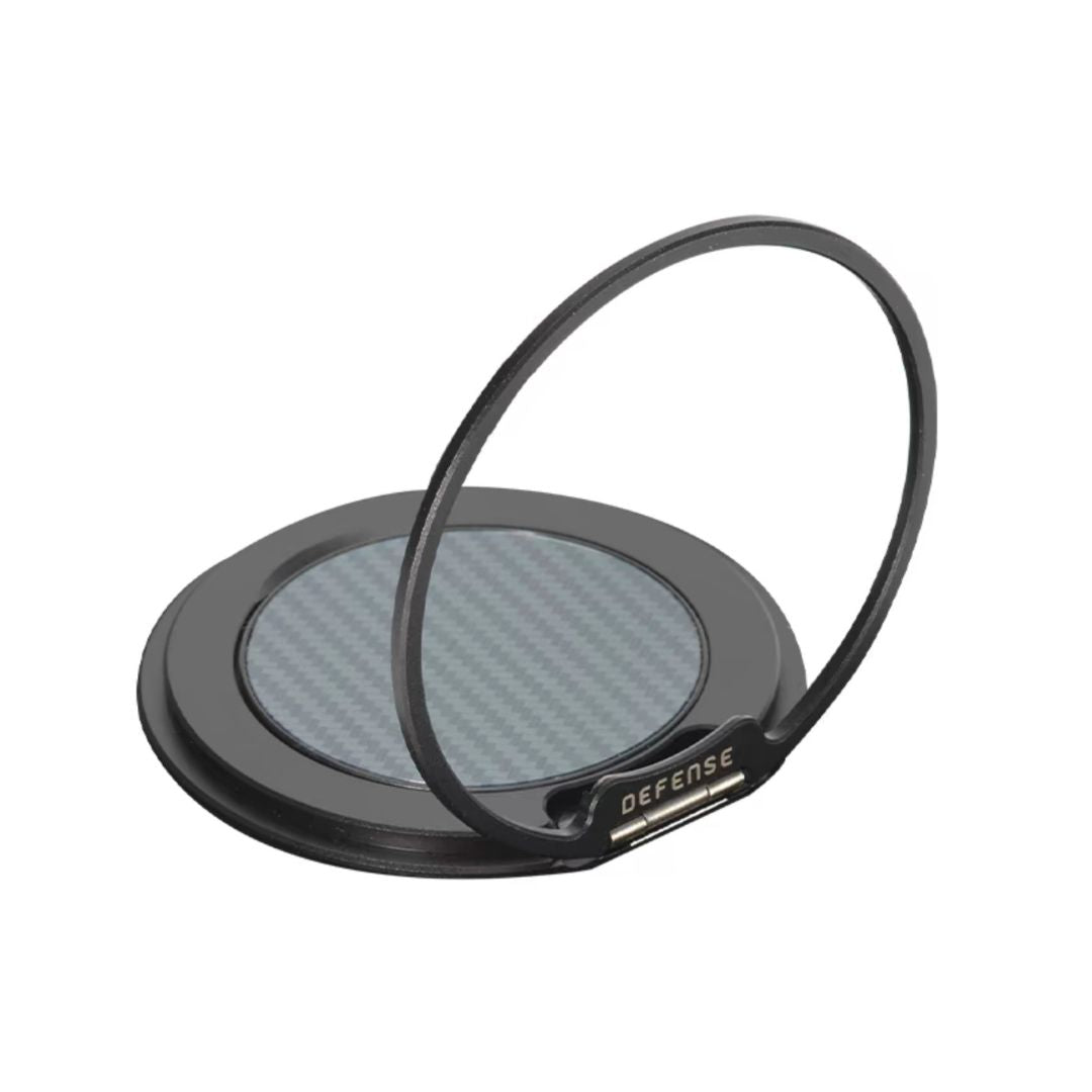 The MobileTechnica Magnetic Ring with Pop holder - Raptic Defense is a black circular phone ring holder featuring a metallic finish, carbon fiber center, and "DEFENSE" engraving. It stands upright as a kickstand against a white background.