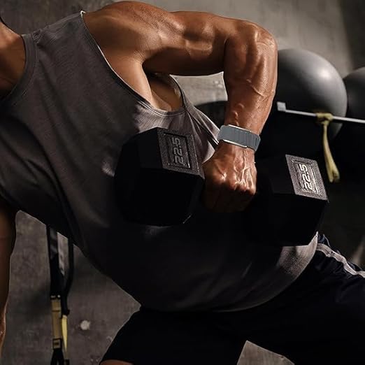 A muscular person wearing a sleeveless shirt and the MobileTechnica Whoop 5.0 Band Silicone Wristband lifts a black 22.5 lb dumbbell in a bent-over row at the gym, with exercise equipment and stability balls in the dimly lit background.