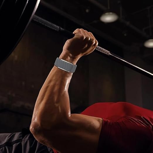 Wearing a MobileTechnica Whoop 5.0 Silicone Wristband with secure, waterproof straps, a person in a bright red shirt grips a barbell on the bench press, their muscular arm highlighted under dim gym lights.