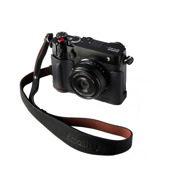 A FUJIFILM GFX100RF camera in the brown SmallRig GFX100RF Leather Case Kit (case, shoulder strap, concave shutter button cap) is angled left to display top dials and buttons, isolated on white.