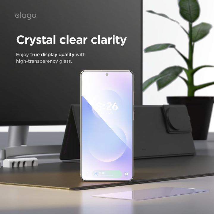 A Samsung Galaxy S26 Ultra upright on a desk showcases the MobileTechnica Elago 2-pack screen protector, offering crystal clear clarity with high-transparency glass. A monitor, charging stand, laptop, and plant sit in the background.