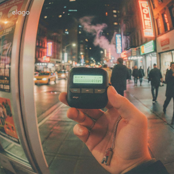 A hand holds the MobileTechnica Samsung Galaxy Buds 4 Pro & Cover in a black pager-style case with lanyard, against a neon-lit city street bustling with taxis and pedestrians. The scene is vibrant and urban.