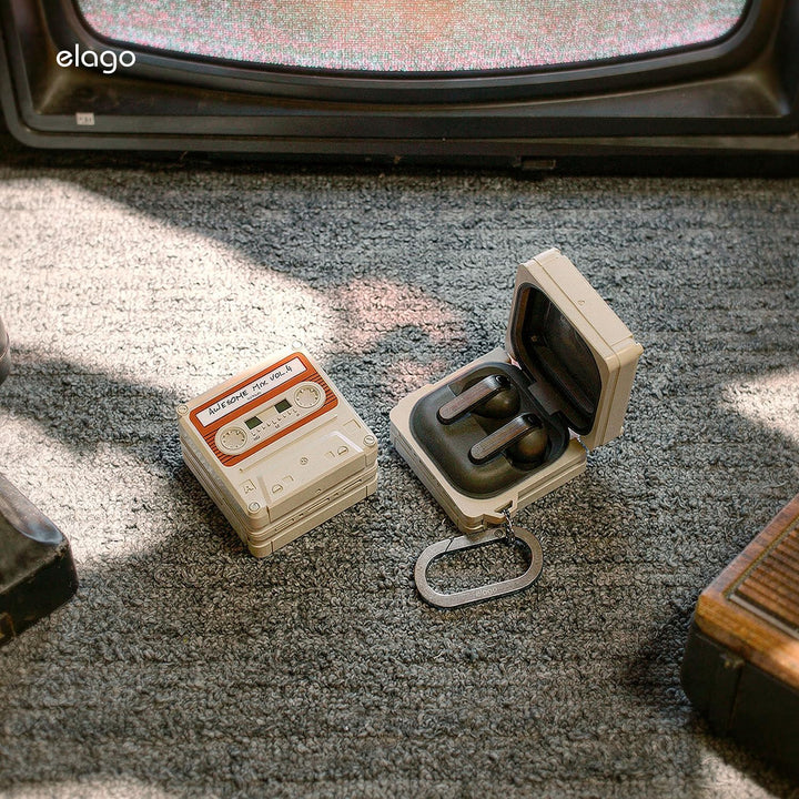 A pair of black Samsung Galaxy Buds 4 Pro rest in a MobileTechnica Galaxy Buds 4 Case, Classic White cassette design with full protection and a carabiner, sunlight highlighting the retro style on the textured carpet.