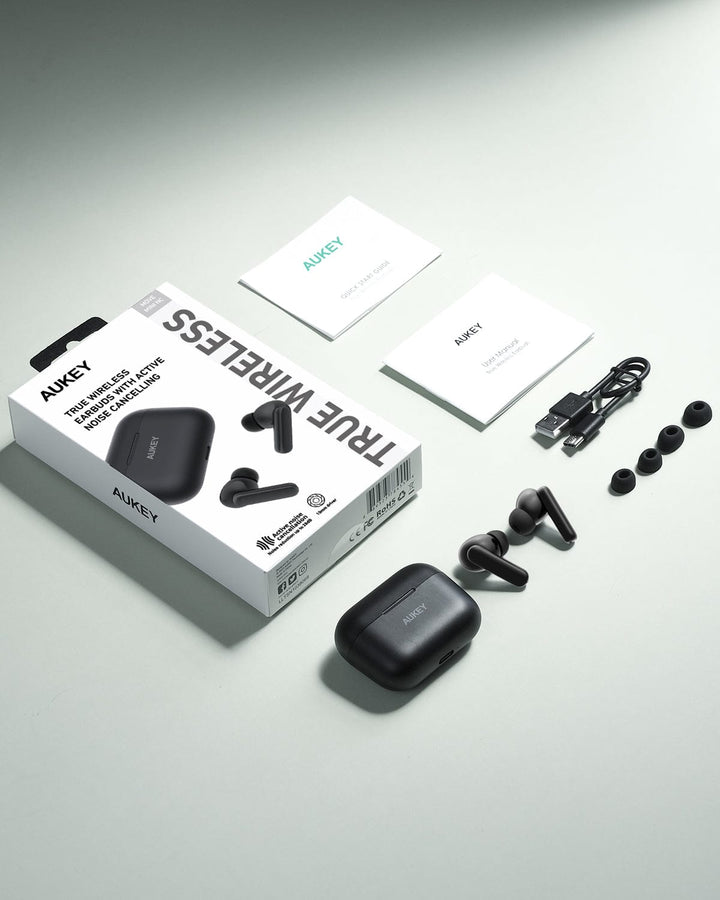 Aukey Active Noise Cancelling Earbuds - Aukey MiniNC with charging case, USB cable, 3 ear tip pairs, manuals, and product box—all neatly arranged on a light gray surface for outstanding sound and clear calls.