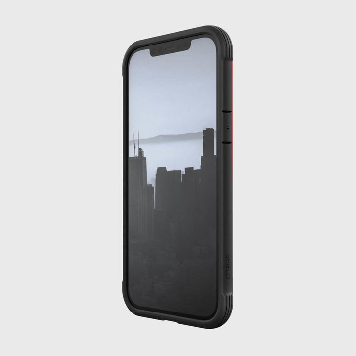 iPhone 12 Pro Max in a Raptic Shield black case with military-grade protection, showcasing a cityscape image on the screen with tall buildings and a hazy sky in the background. Drop tested for durability.