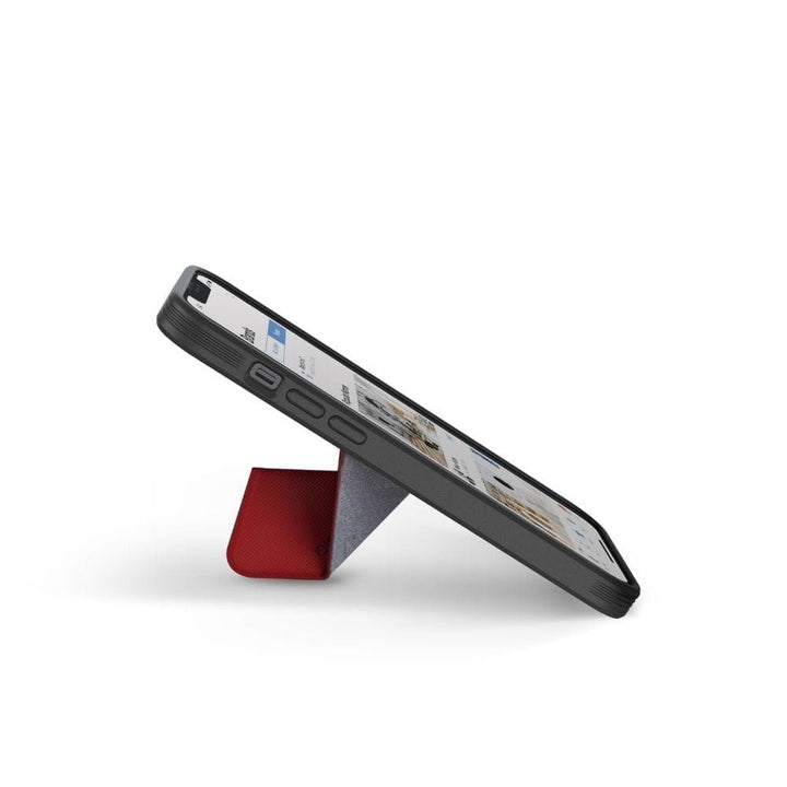 An iPhone 13, equipped with the UNIQ Transforma MagSafe Folding Case, is placed in landscape mode on a slim, triangular red stand. The screen displays a website with text and image thumbnails. The black case from UNIQ provides drop protection, while the white background highlights the minimalist design of this hands-free setup.